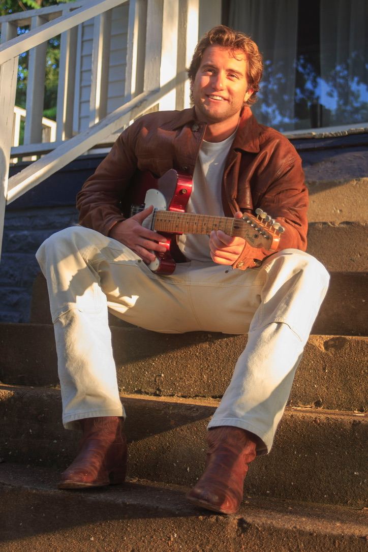 Dante smiling on concrete steps with a red electric guitar