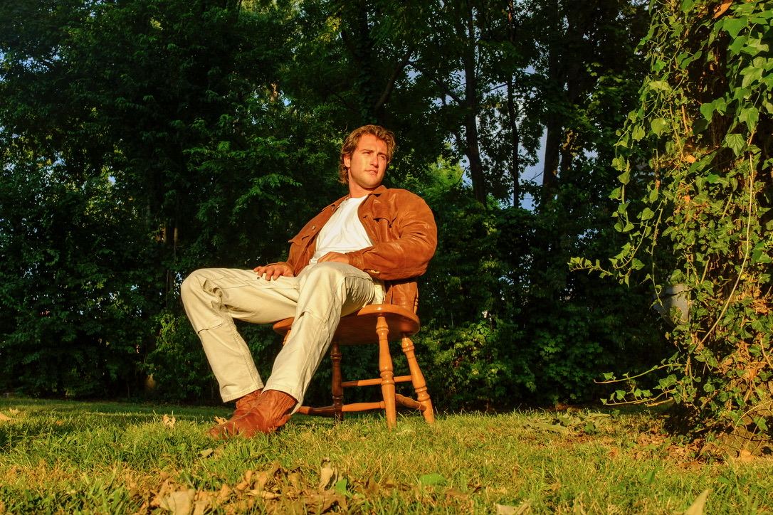 Dante leaning back in a wooden chair on a grassy lawn surrounded by trees