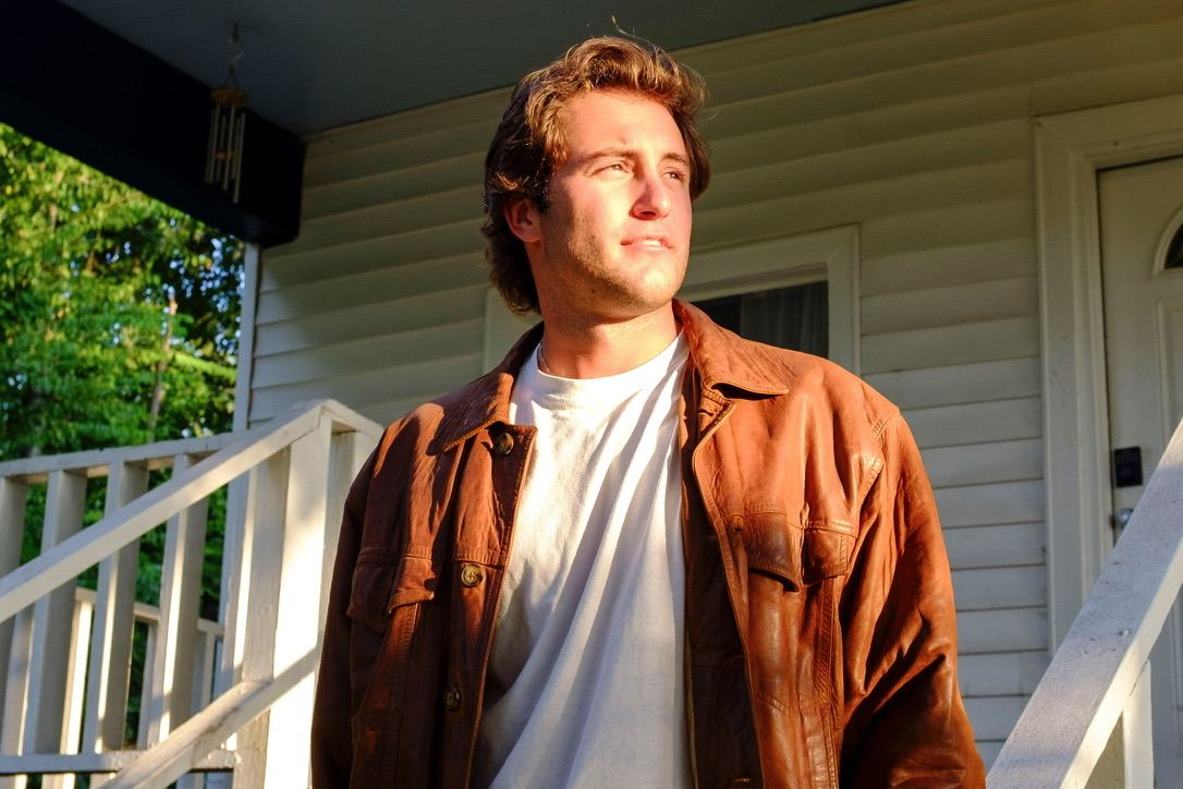 Dante in a brown leather jacket, looking off to the side in golden evening light on a porch