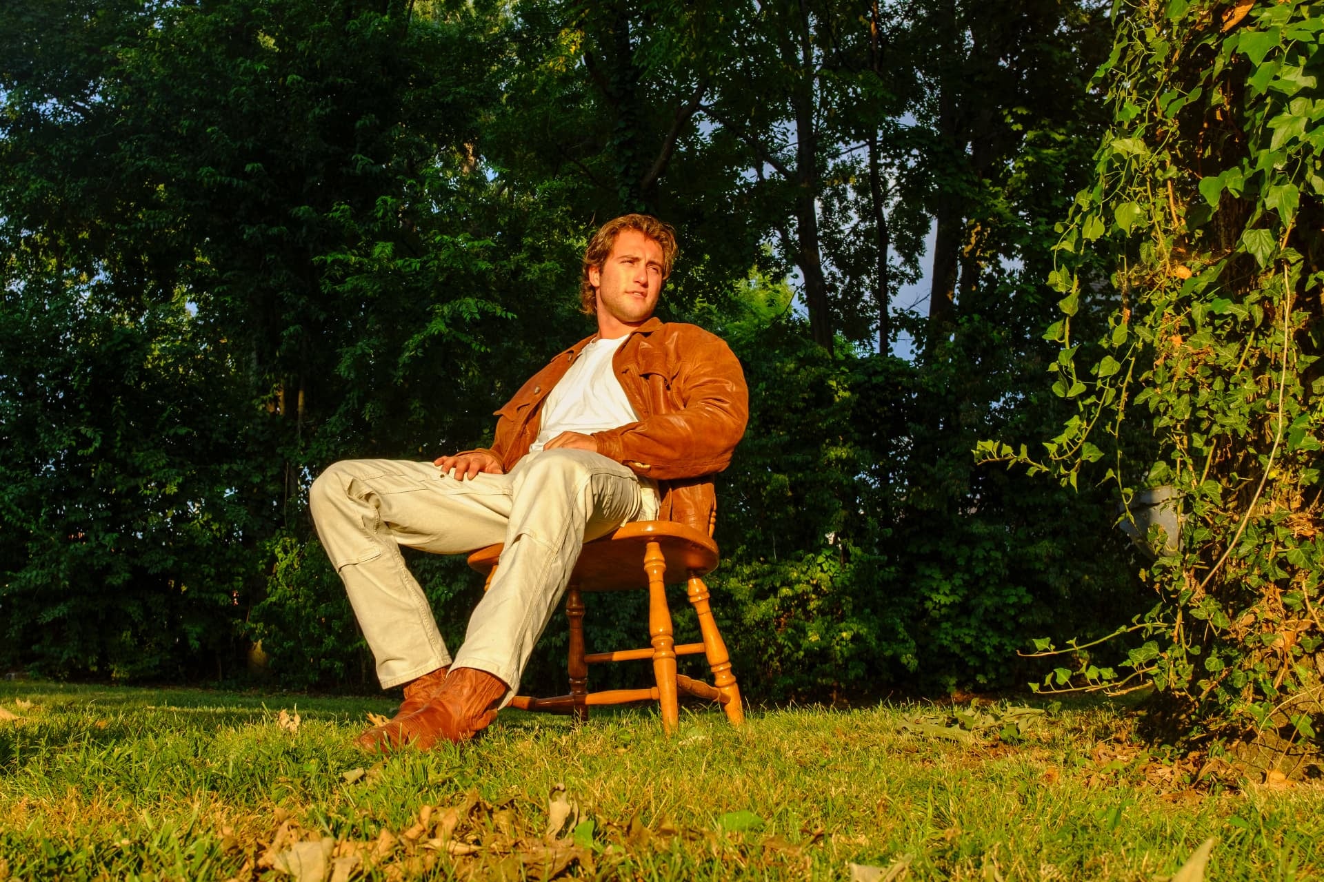 Dante leaning back in a wooden chair on a grassy lawn surrounded by trees
