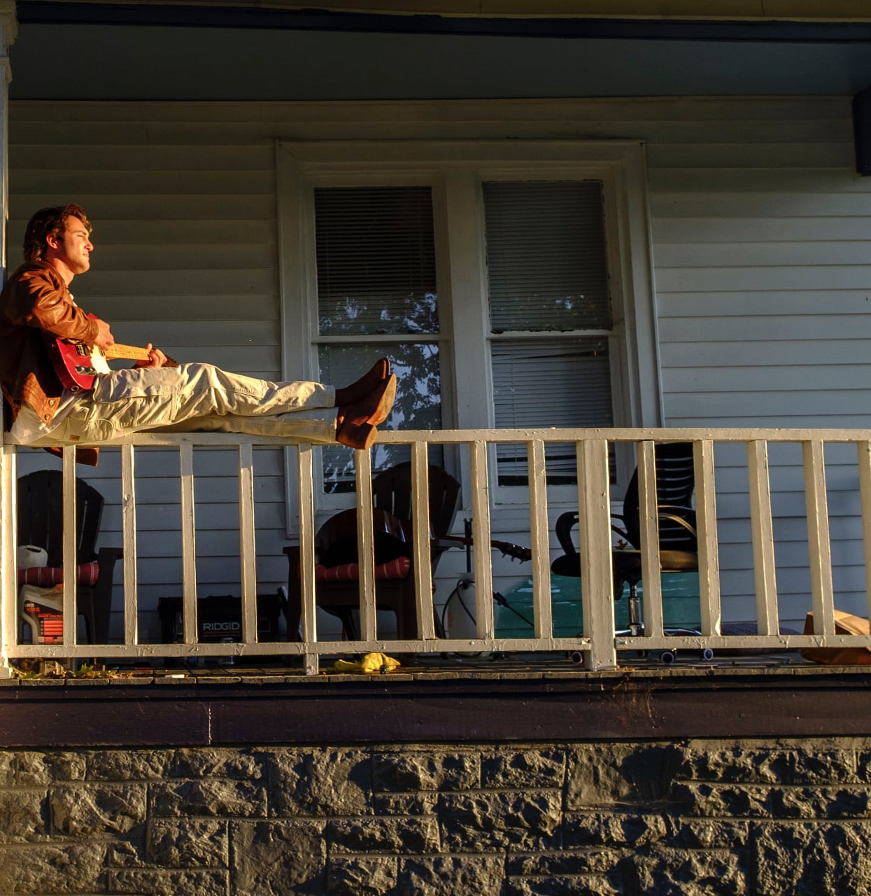 Dante DeRosa sitting on a porch railing at golden hour playing his red Telecaster