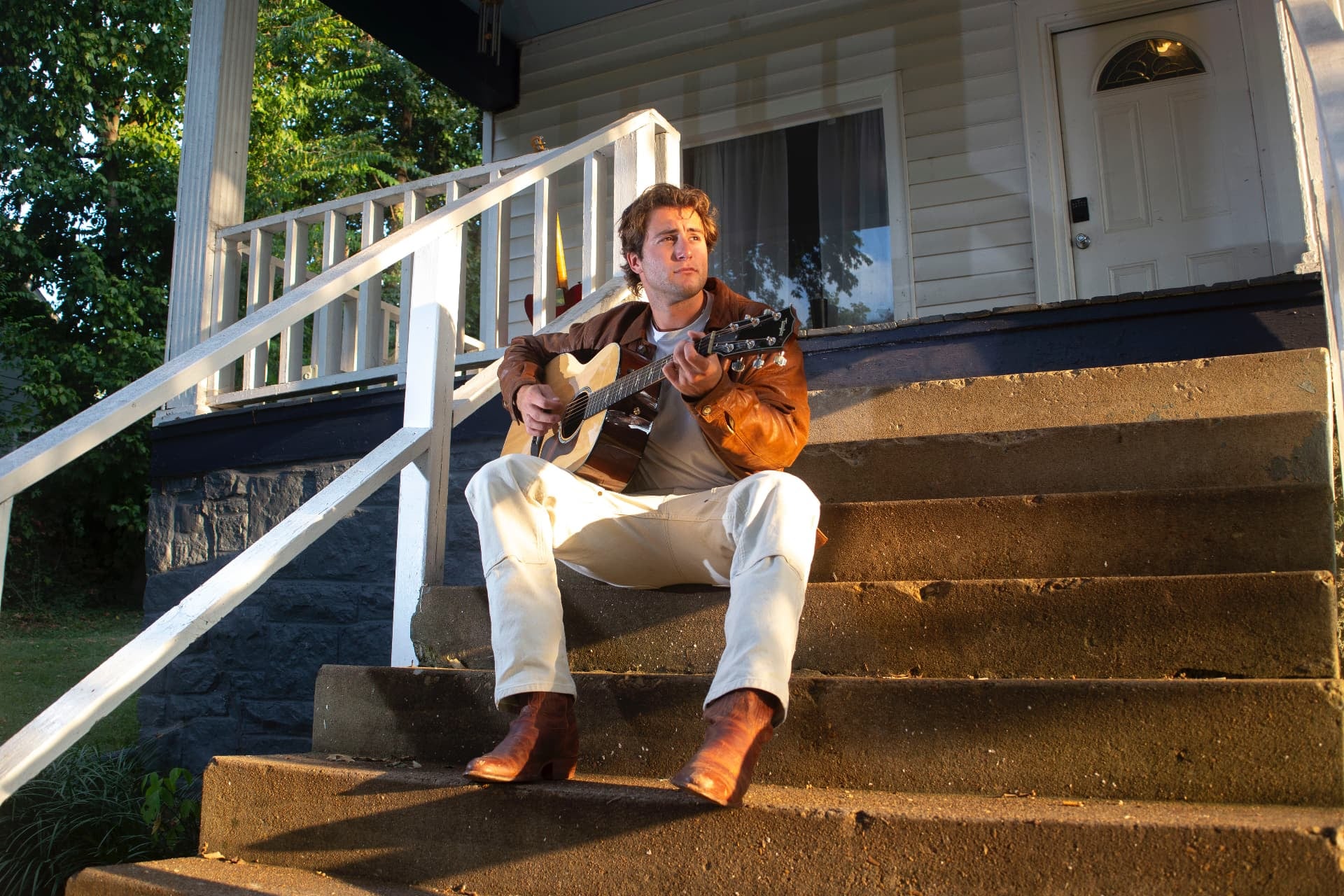Dante DeRosa sitting on porch steps at golden hour playing an acoustic guitar
